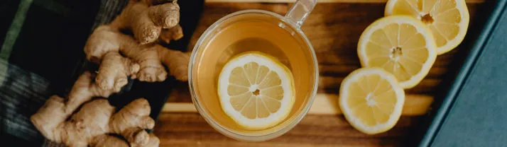 Une tasse de grog chaud avec une rondelle de citron, posée sur une planche en bois entre des racines de gingembre frais et des rondelles de citron.