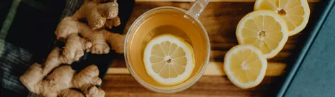 Une tasse de grog chaud avec une rondelle de citron, posée sur une planche en bois entre des racines de gingembre frais et des rondelles de citron.