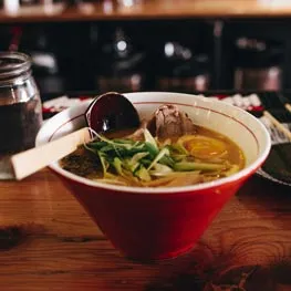 Un bol de bouillon aux nouilles, à l’œuf et aux oignons nouveaux, posé sur un comptoir en bois.