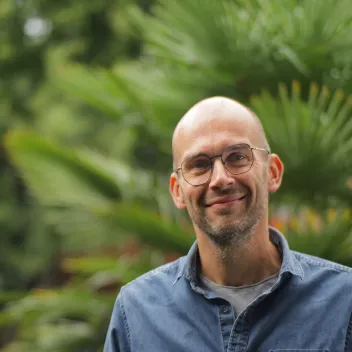 M. Duponchel en extérieur, en chemise en jean et lunettes, souriant devant un fond de feuillage.