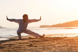 Une personne qui pratique un mouvement de qi gong en plein air, au bord de l’eau.