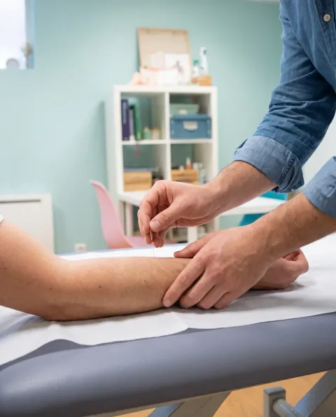 Deux mains, manches en jean retroussées, posent une aiguille fine sur un avant-bras, sur la table de soin.