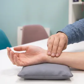 Trois doigts posés sur un poignet reposant sur un petit coussin gris, sur le bureau blanc du cabinet.