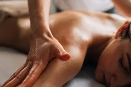 Des mains qui massent le haut du dos d’une personne allongée.